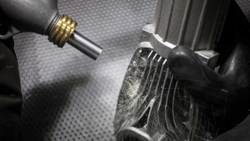 Nozzle blasting a metal part with small particles.