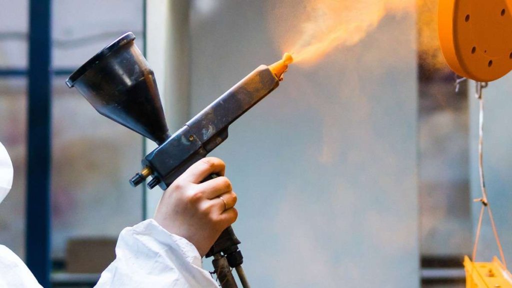 Spray gun applying powder coating to a part.