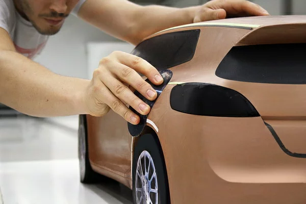 Person shaping a clay model of a car during automotive prototyping.