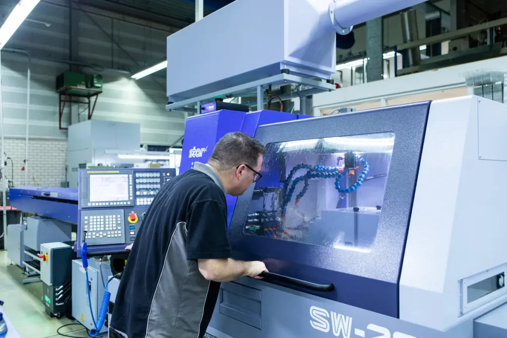 A man examines a machine in a modern factory setting, with control panels and other equipment.
