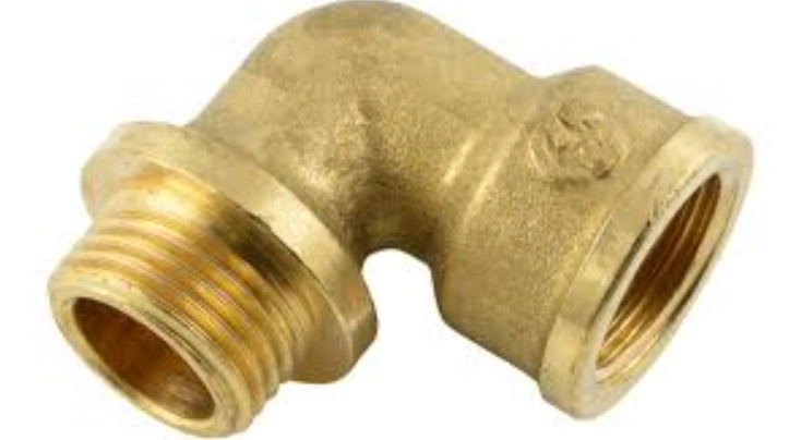 A closeup of a 90° elbow of yellow brass with male and female threads on opposite ends