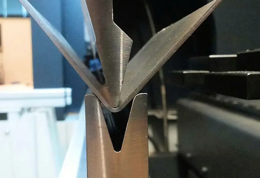 Close-up of sheet metal being formed in a press brake V-die into an acute bend angle