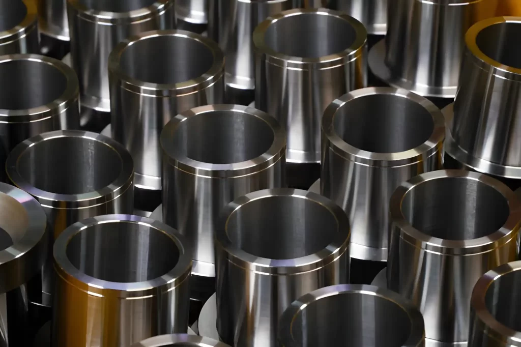 Multiple shiny steel machined parts are arranged in bulk in a workshop after production.