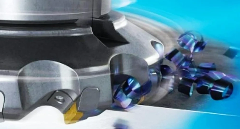 A closeup image of side CNC milling operation showing a rotating cutter with inserts and some machined chips 
