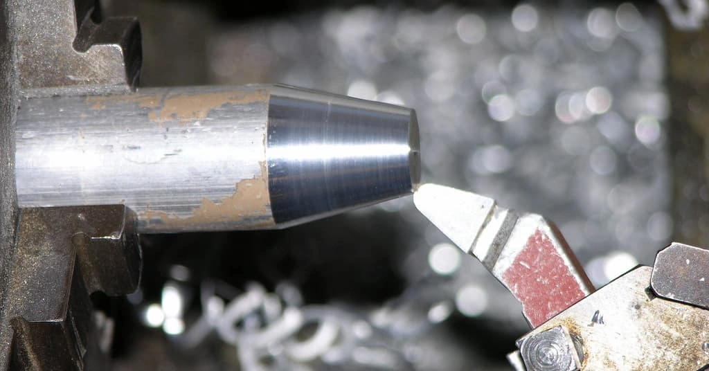 A close-up view of a cutting tool tapering the cylindrical work on the lathe machine