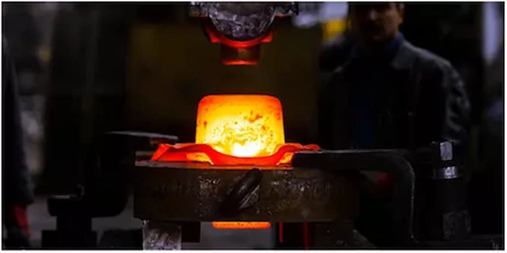 A close-up view of the heat treatment setup; the punch is about to strike the hot-red titanium placed over the die. 